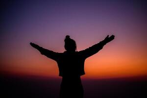 Silhouette of cheering hiking woman open arms to the sunrise stand on mountain photo