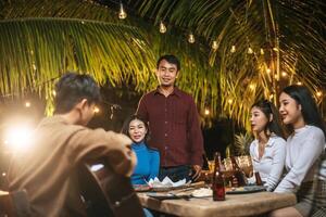 Portrait of Happy Asian group of friends having fun to music dining and drinking together outdoor - Happy friends group toasting beers  - People, food, drink lifestyle, new year celebration concept. photo