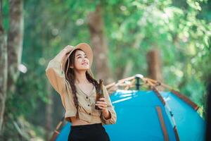 Young woman cheer and drink beverage  front of camping tent photo