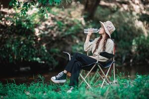 Young pretty woman sitting and drink water near stream photo