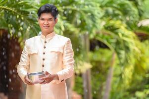 Young man splashing water from bowl on Songkran festival photo