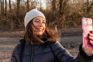 medio Envejecido mujer vistiendo invierno ropa tomando un selfie por un río foto