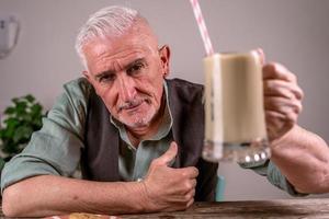 casual dressed mature man with sunglasses sitting at a table drinking iced coffee photo