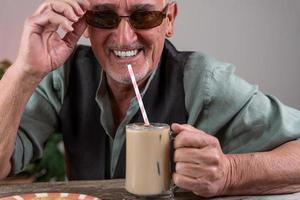 casual dressed mature man with sunglasses sitting at a table drinking iced coffee photo