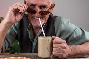 casual dressed mature man with sunglasses sitting at a table drinking iced coffee photo