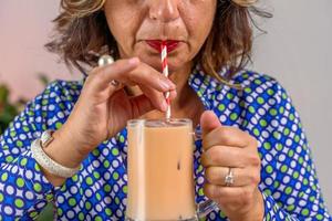 woman dressed in blue shirt sitting drinking cold coffee through a straw photo