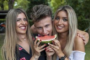 three young and beautiful people they eating a slice of fresh and juicy watermelon photo