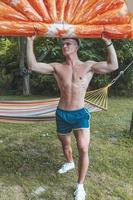 young muscular adult posing with an orange slice-shaped air mattress photo