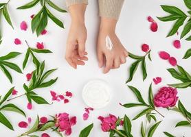 two female hands and a jar with thick cream and burgundy flowering peonies photo