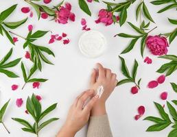 two female hands and a jar with thick cream and burgundy flowering peonies photo