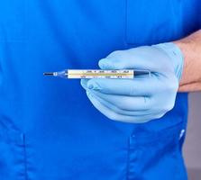 doctor with blue latex gloves and uniform holding a glass mercury thermometer photo