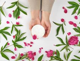 two female hands and a jar with thick cream and burgundy flowering peonies photo