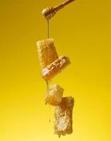 pouring transparent sweet honey from a wooden stick on a wax honeycomb. Yellow background photo