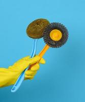 hand in a yellow glove holds a stack of plastic cleaning brushes, blue background photo