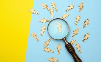 wooden men and a magnifying glass on a blue background. Recruitment concept, search for talented and capable employees photo