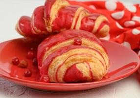 baked croissant with cherry glaze on a red ceramic plate photo