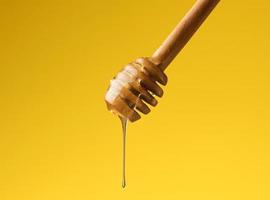 pouring transparent sweet honey from a wooden stick. Yellow background. Food levitates photo