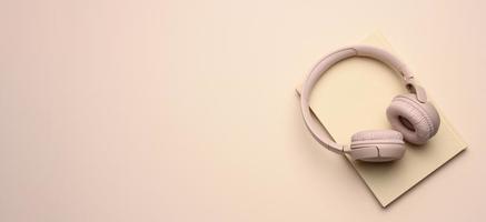 beige wireless headphones and a closed notepad on a beige background, banner photo