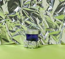 frasco de vidrio azul con tapa de plástico gris para cosméticos sobre un fondo abstracto con lámina arrugada. marca de productos cosméticos crema, máscara, suero foto
