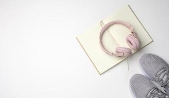 pink wireless headphones, a pair of sneakers and a notepad on a white background, top view. Womens clothing photo