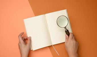 open paper notebook with blank white sheets and a wooden magnifier on a orange background photo