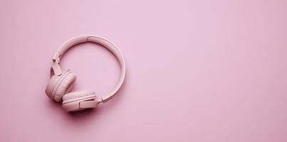 pink wireless headphones on a pink background, banner. Top view on modern gadget photo