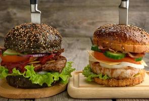 two cheeseburgers with vegetables and meat steak on a wooden board photo