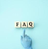 female hand in a blue latex glove points to wooden blocks with the inscription  FAQ frequently asked questions on a blue background photo