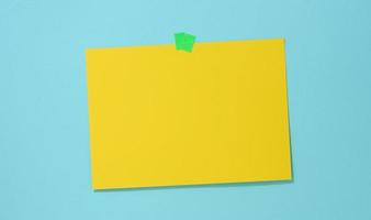 blanco rectangular amarillo sábana de papel pegado en un azul antecedentes. sitio para un inscripción, anuncio foto