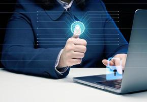 a woman sits at a table and works at a laptop. The hand presses a virtual button to scan the fingerprint. The concept of personal data protection photo