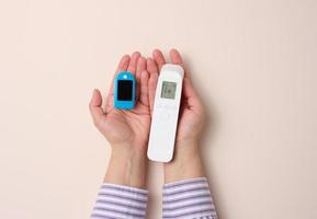 female hand holds plastic non-contact thermometer and oximeter on beige background photo