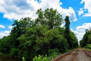 árboles verdes junto al lago día soleado, con nubes en el cielo camino de rieles de ferrocarril foto