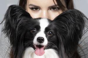 A cute young woman is hugging her papillon puppy. The eyes of a beautiful girl and the eyes of a funny dog with big ears. photo