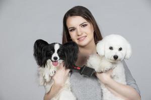A cute young woman is holding her papillon and bichon puppy. Love between owner and dog. The girl plays with the dogs. Pets. photo