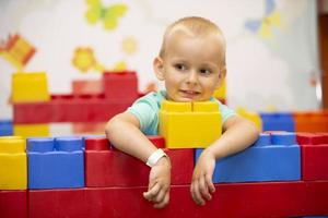 A little boy plays with a lot of colorful plastic construction blocks and builds indoors. photo