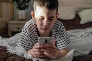 The boy lies on the bed and watches a cartoons and video on a smartphone photo