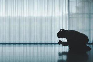 silhouette of woman kneeling and praying in modern church at sunset time. Female catholic prayer worship to God wish a better life in home at dawn with believe faith. concept of worshipers kneeling. photo