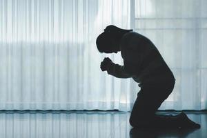 silhouette of woman kneeling and praying in modern church at sunset time. Female catholic prayer worship to God wish a better life in home at dawn with believe faith. concept of worshipers kneeling. photo