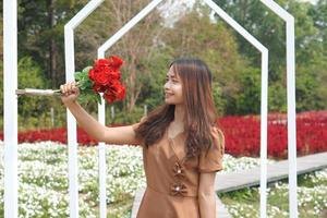 asiático mujer sonriente felizmente entre hermosa flores foto