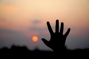 silueta de humano mano elevado a hacer un desear, puesta de sol antecedentes foto