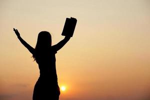 silhouette of a woman holding a computer sunset background photo