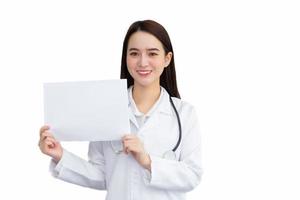 Asian woman professional doctor who wears medical coat standing confidently smiling and holds shows white paper to present something isolated on white background in healthcare concept. photo