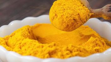 Detail shot of turmeric root powder in a wooden spoon on table . video