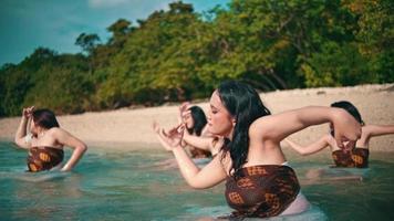 ein Gruppe von asiatisch Frauen im braun Kleider ist genießen das Blau Meer Wasser durch Tanzen mit ihr freunde auf das Strand auf ein Insel video