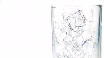 refrigerantes são derramados sobre cubos de gelo em um copo transparente, espumando e dispersando. video