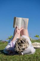 mujer acostada y leyendo su libro favorito en un prado cubierto de hierba verde fresca en un día soleado de verano o primavera. foto