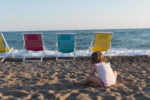 niña sentada en la arena y jugando con balde y pala en la playa del mar en un cálido día soleado de verano. de cerca. vista lateral. foto