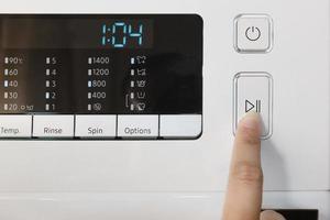 Closeup of female hand touching digital screen, automatic washing machine control panel, start or pause button. photo