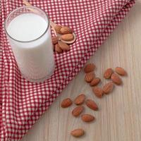 almond milk in glass and spoon with nuts are around on red cloth on wood background. selective focus.top view, top-down, flatlay. photo