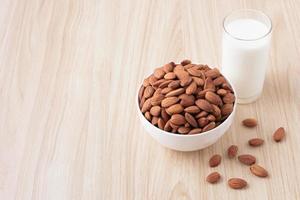 nueces de almendra en un tazón blanco y leche en vidrio sobre fondo de madera con nueces alrededor del tazón. enfoque selectivo. vista frontal. espacio de copia. foto